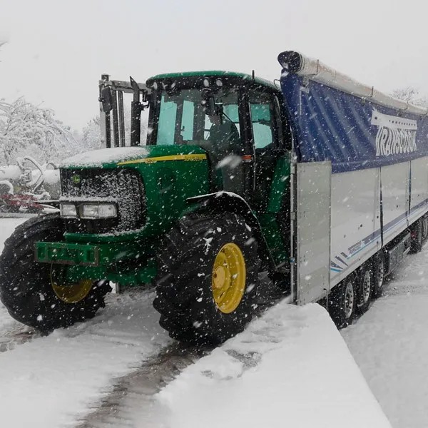 Tracteur vert à côté d’une semi-remorque Transcosur par un jour de neige